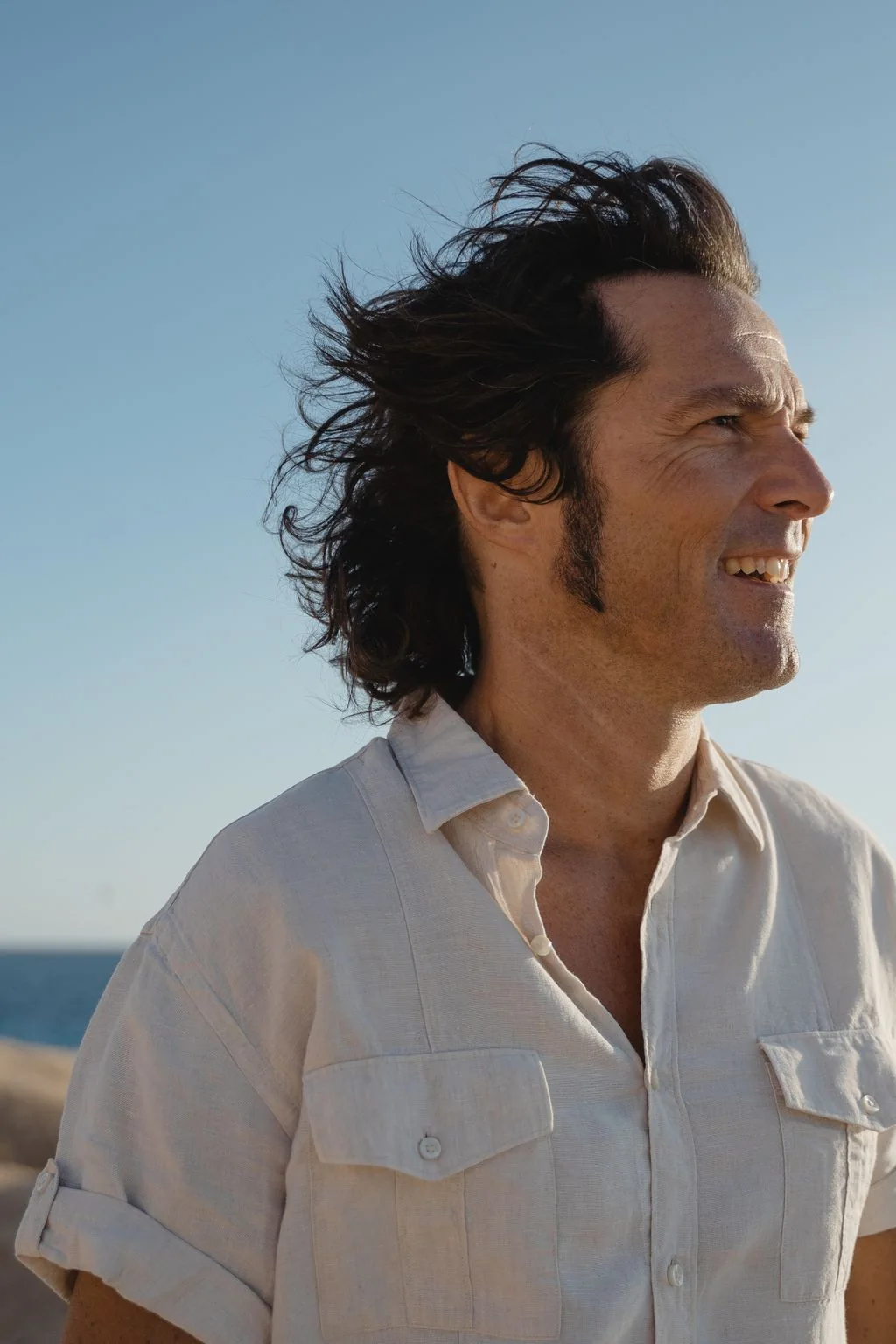 A confident man with a full head of hair standing by the coast